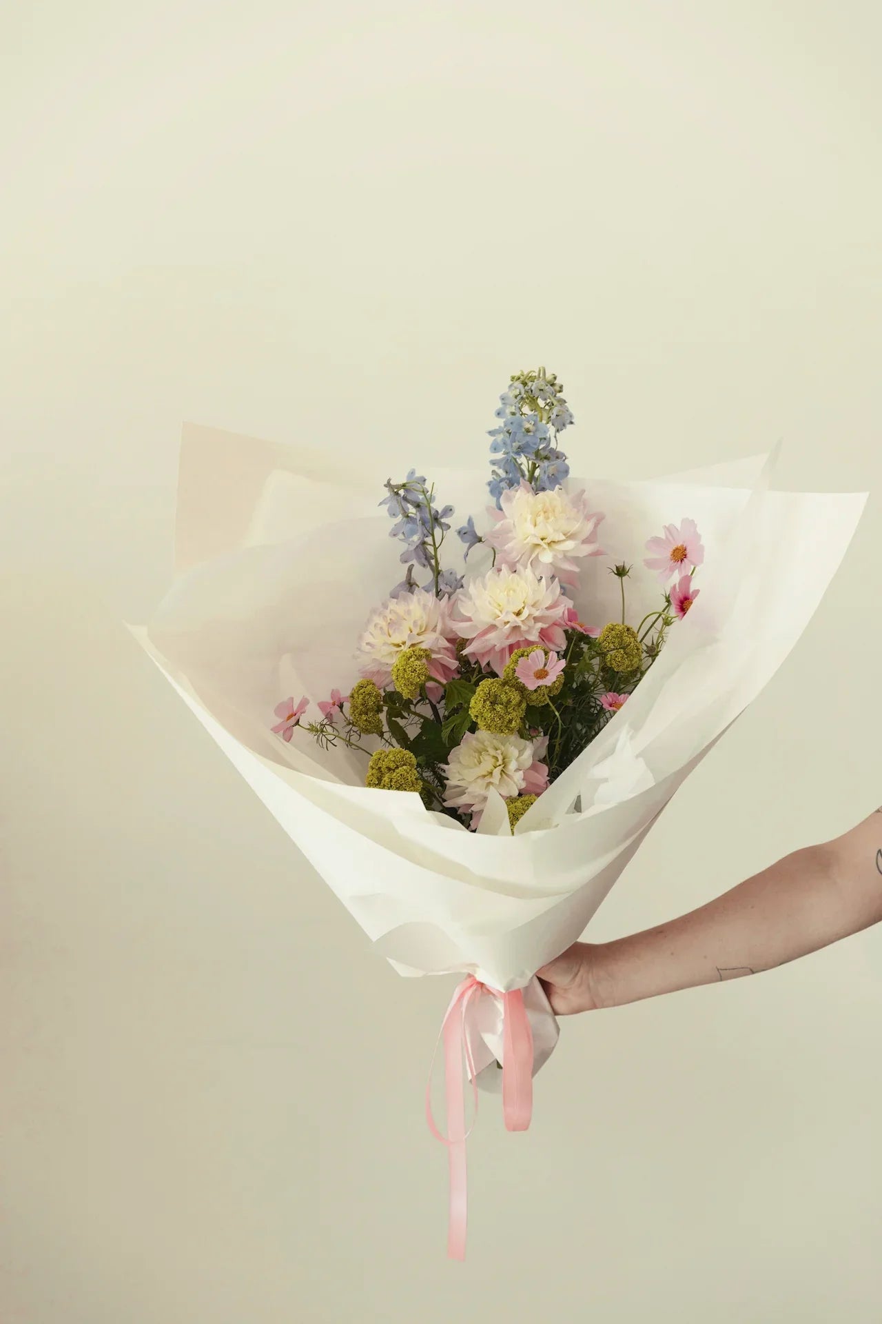 Hand holding pastel flower bouquet with blue, pink, and white blooms in white wrap