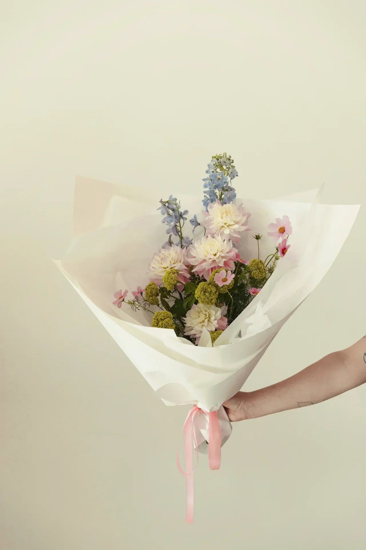Fresh seasonal bouquet with pastel flowers wrapped in white paper and pink ribbon
