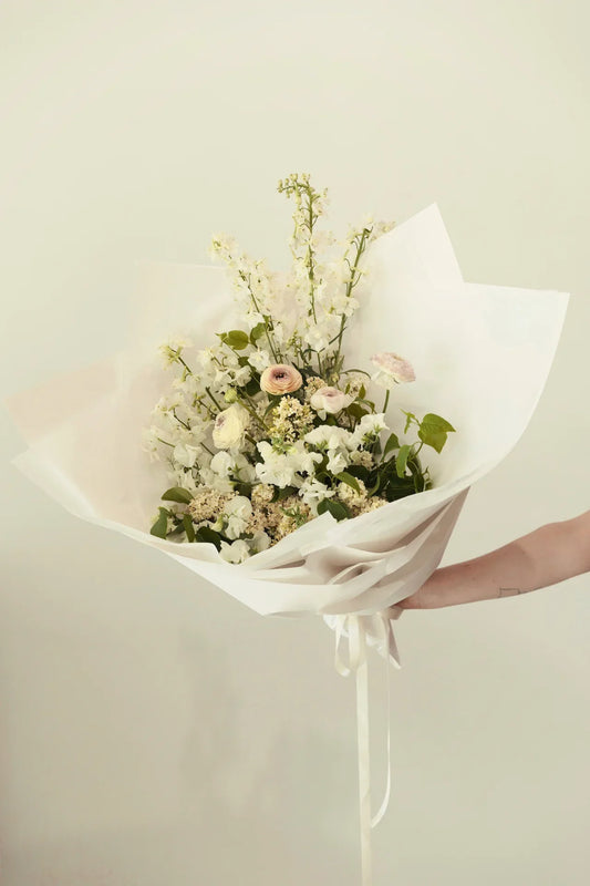 Hand holding elegant white flower bouquet with greenery wrapped in white paper