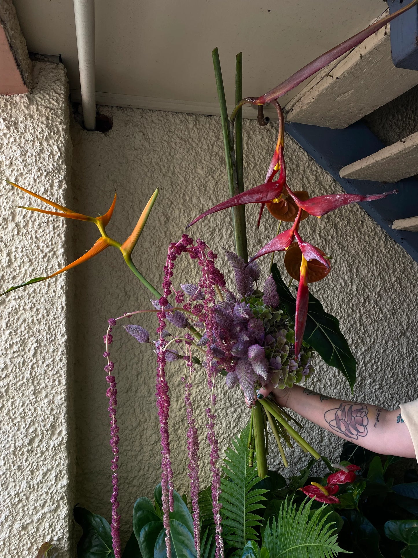 Hand holds tropical flower bouquet with heliconia, pink amaranthus, and lush greenery