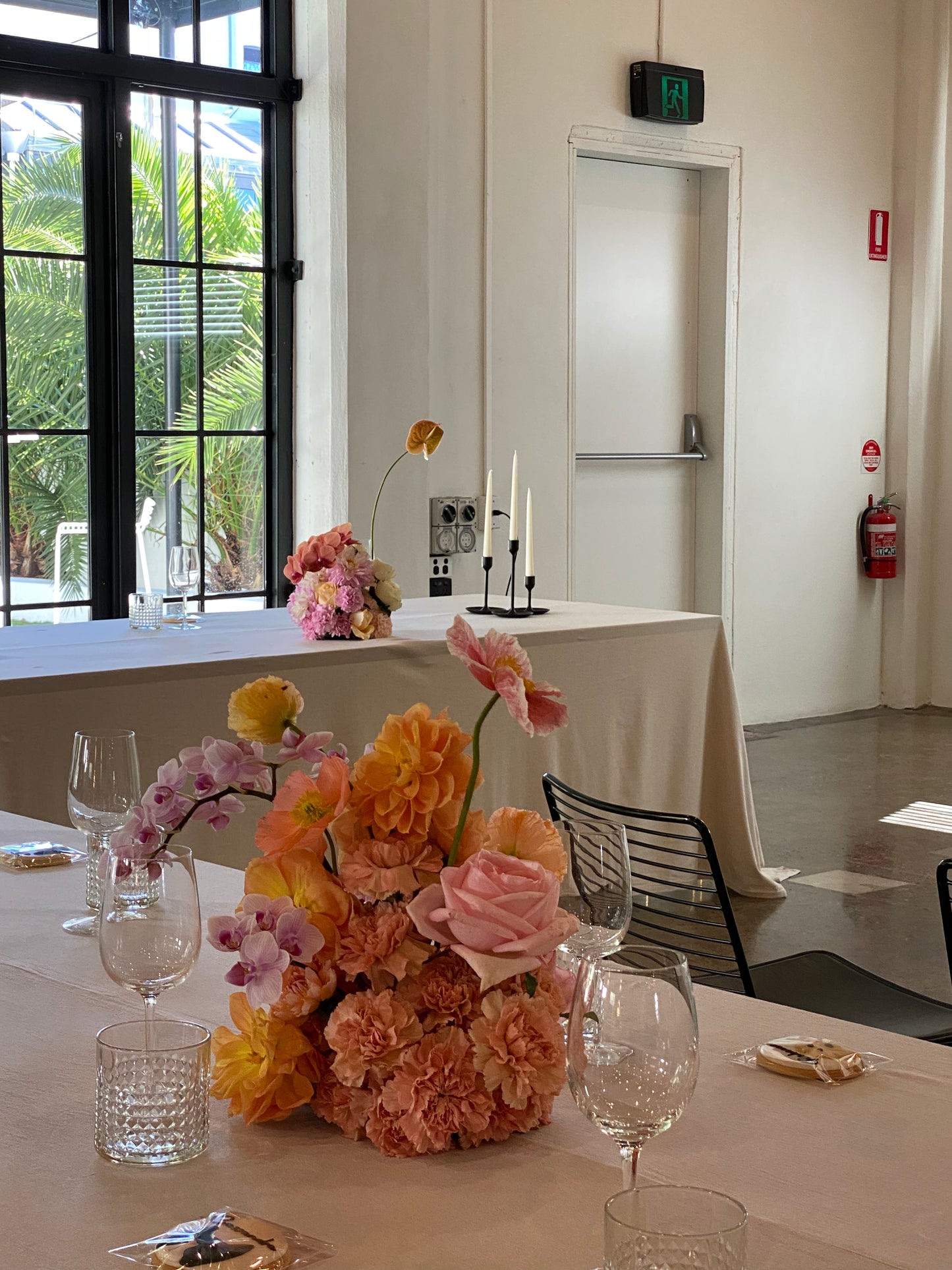 Elegant table setting with pastel floral arrangement, wine glasses, and candles in a bright event space