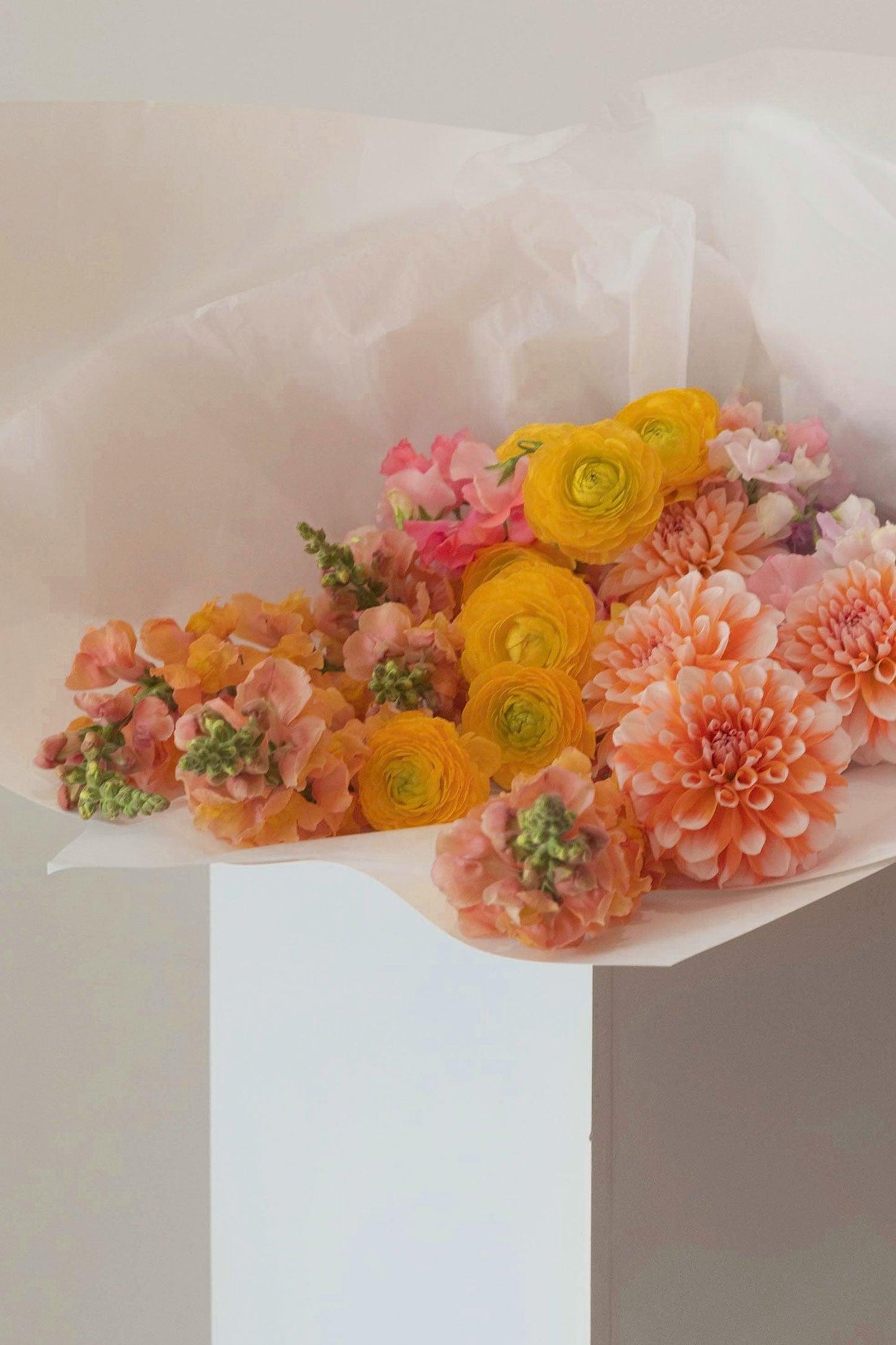 Close-up of bright flower bouquet with yellow ranunculus and peach dahlias on white paper