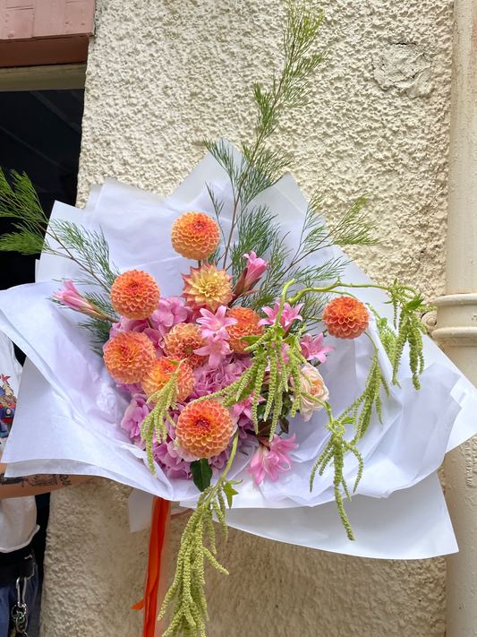 Vibrant bouquet of orange and pink flowers with green foliage, wrapped in white paper