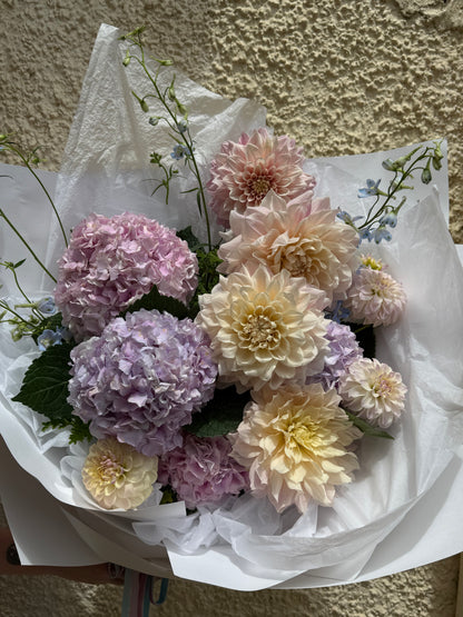 Bouquet of flowers wrapped in white paper against a textured wall.